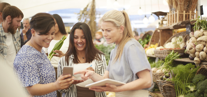 Women talking at a farmers market with a smart phone and tablet.